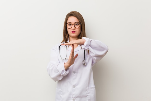 Junge Doktorfrau gegen eine weiße Wand, die eine Auszeitgeste zeigt.