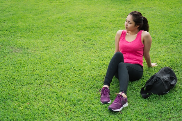 Junge Eignungsfrau, die draußen für Entspannung im Park nach Training und Lauf sitzt.