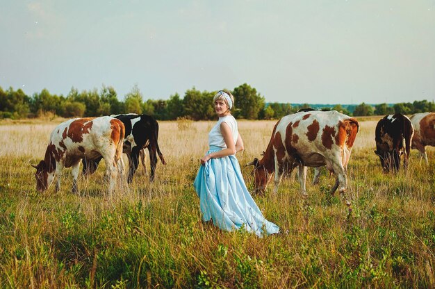 Junge, elegante, glückliche Frau, die in der Natur spazieren geht, Dorf. Weide, Wiese. Kühe. Ländliche Landschaft