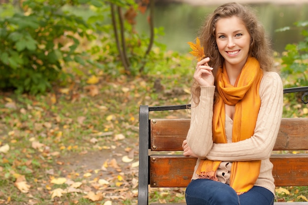 Junge elegante lockige Frau mit Herbstlaub