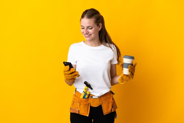 Junge Elektrikerfrau lokalisiert auf gelbem Hintergrund, der Kaffee hält, zum weg und ein Handy