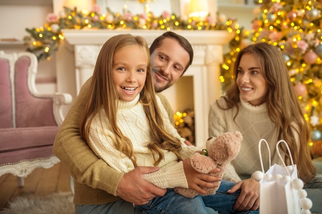 Junge Eltern geben Weihnachtsgeschenk zu ihrer Tochter und Familie, die glücklich schauen