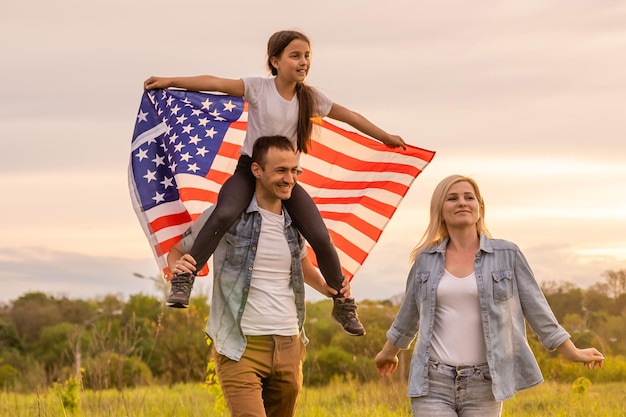 Junge Eltern mit ihrer Tochter, die bei Sonnenuntergang die amerikanische Flagge auf dem Land hält. Feier zum Unabhängigkeitstag.