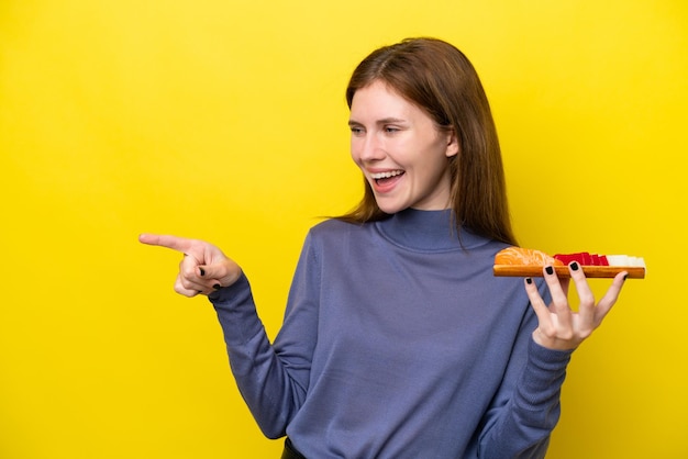 Junge Engländerin hält Sashimi isoliert auf gelbem Hintergrund, zeigt mit dem Finger zur Seite und präsentiert ein Produkt