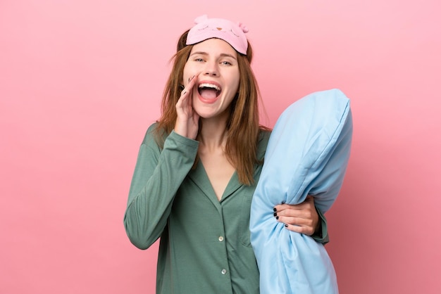 Junge Engländerin im Schlafanzug isoliert auf rosa Hintergrund im Schlafanzug und schreiend mit weit geöffnetem Mund