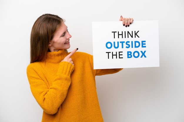 Junge Engländerin isoliert auf weißem Hintergrund, die ein Plakat mit dem Text Think Outside The Box hält und darauf zeigt