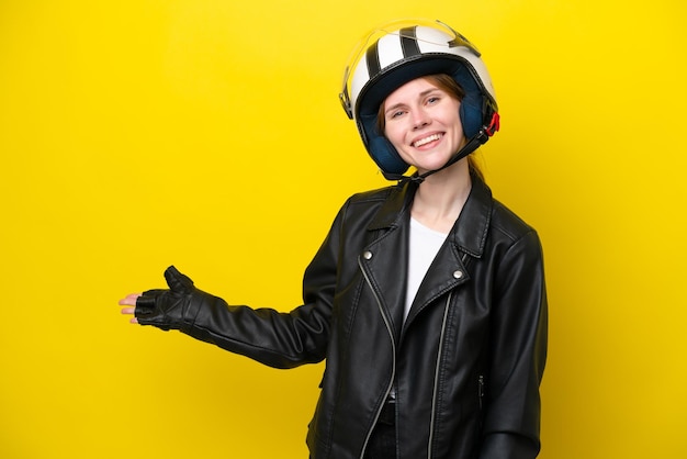 Junge Engländerin mit einem Motorradhelm isoliert auf gelbem Hintergrund, der die Hände zur Seite ausstreckt, um zum Kommen einzuladen
