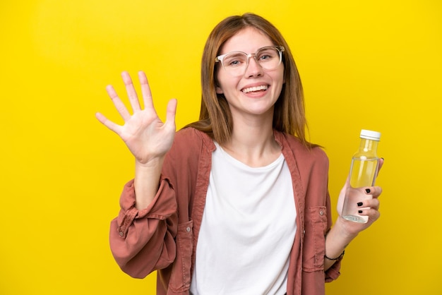 Junge Engländerin mit einer Flasche Wasser isoliert auf gelbem Hintergrund, die fünf mit den Fingern zählt