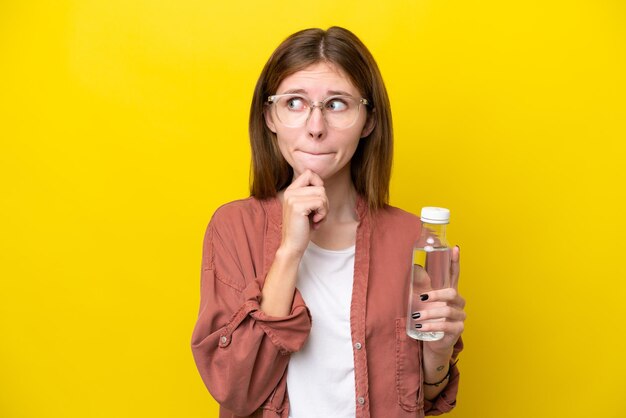 Junge Engländerin mit einer Flasche Wasser isoliert auf gelbem Hintergrund, die Zweifel hat und nachdenkt