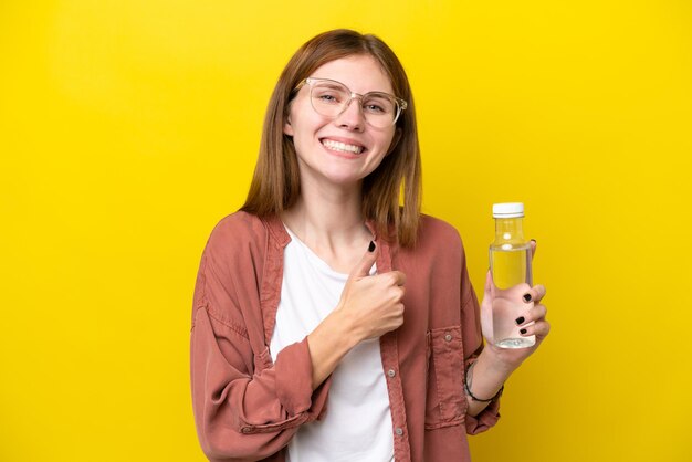 Junge Engländerin mit einer Flasche Wasser isoliert auf gelbem Hintergrund mit einer Daumen hoch Geste