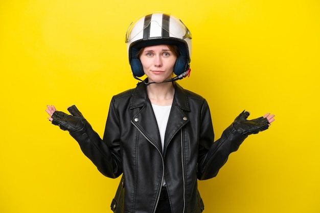 Junge Engländerin mit Motorradhelm isoliert auf gelbem Hintergrund, die Zweifel hat, während sie die Hände hebt