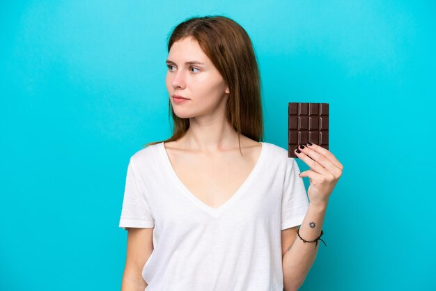 Junge Engländerin mit Schokolade isoliert auf blauem Hintergrund zur Seite schauend