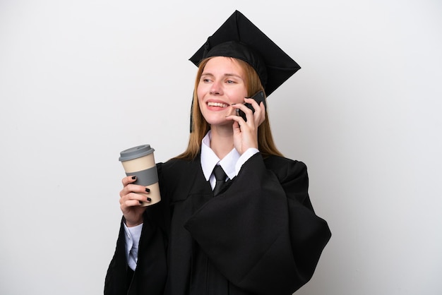 Junge Engländerin mit Universitätsabschluss isoliert auf weißem Hintergrund mit Kaffee zum Mitnehmen und einem Handy