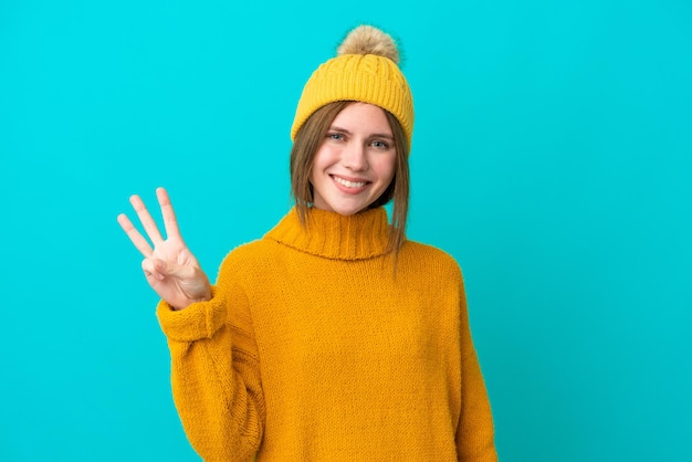 Junge Engländerin trägt Winterjacke isoliert auf blauem Hintergrund glücklich und zählt drei mit den Fingern