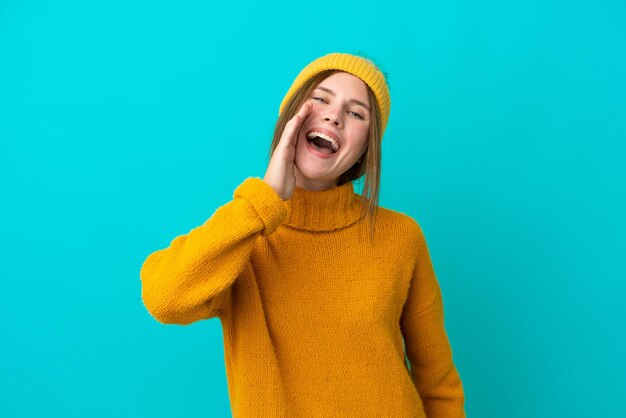 Junge Engländerin trägt Winterjacke isoliert auf blauem Hintergrund und schreit mit weit geöffnetem Mund