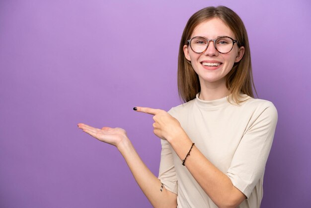 Junge englische Frau lokalisiert auf lila Hintergrund, der imaginären Copyspace auf der Handfläche hält, um eine Anzeige einzufügen