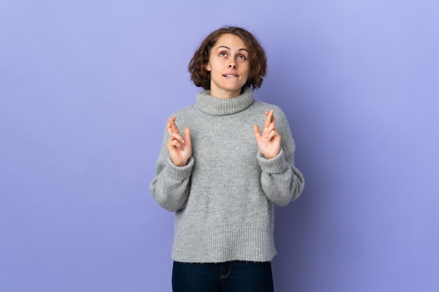 Junge englische Frau lokalisiert auf lila Wand mit den Fingern, die kreuzen und das Beste wünschen