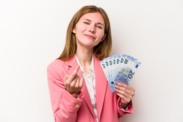 Junge englische Geschäftsfrau, die Banknoten isoliert auf weißem Hintergrund hält und mit dem Finger auf Sie zeigt, als würde sie einladen, näher zu kommen