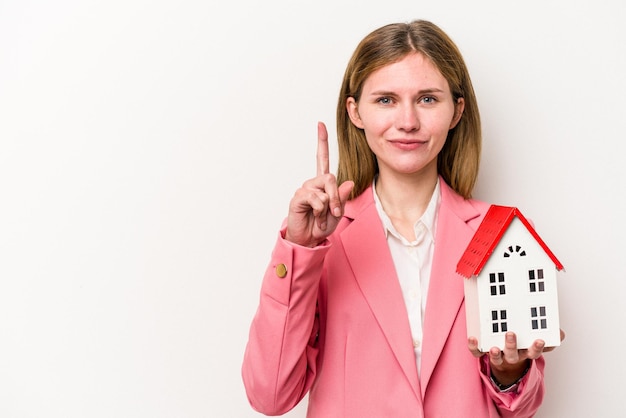 Junge englische Geschäftsfrau, die Hausspielzeug lokalisiert auf weißem Hintergrund hält, der Nummer eins mit dem Finger zeigt