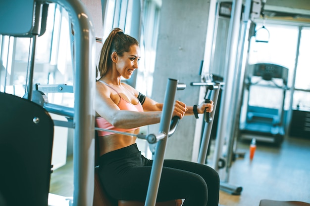 Junge entschlossene Fitnessfrau, die Übungen an der Brustpressmaschine im modernen Fitnessstudio macht