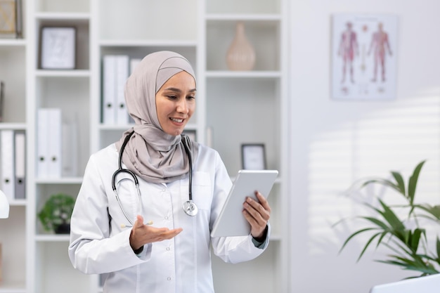 Junge erfahrene Ärztin im Hijab nutzt Tablet-Computer für Videoanrufe. Klinikmitarbeiterin