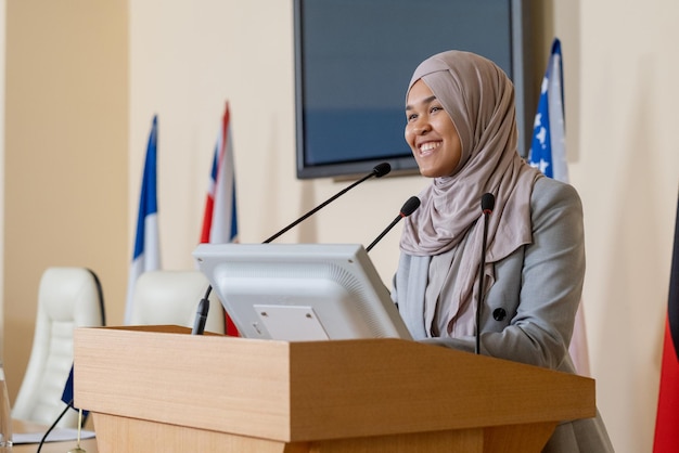 Junge erfolgreiche muslimische Geschäftsfrau im Hijab, die auf der Tribüne steht