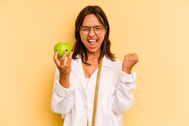 Junge Ernährungswissenschaftlerin, die eine Waage isoliert auf gelbem Hintergrund hält