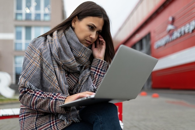 Junge ernsthafte Geschäftsfrau konzentrierte sich auf die Arbeit an Laptops vor dem Hintergrund der Stadt in