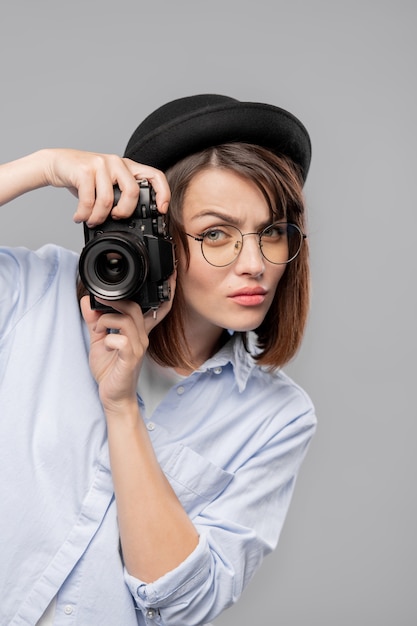 Junge ernsthafte weibliche Fotografin mit Kamera, die sich auf das Fotografieren konzentriert, während sie isoliert steht