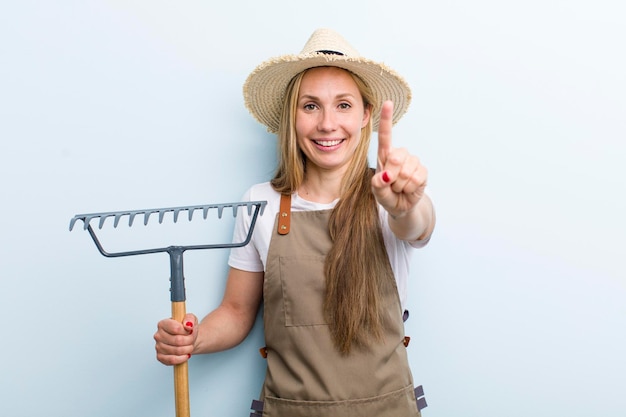 Junge erwachsene blonde Bäuerin mit einem Rechen