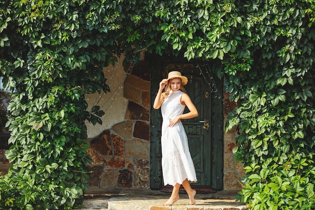 Junge erwachsene Blondine in einem weißen Kleid mit Äpfeln am Saum im Garten des Hauses