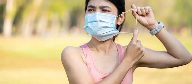 Junge erwachsene Frau, die schützende Gesichtsmaske während des Streckmuskels im Park im Freien trägt