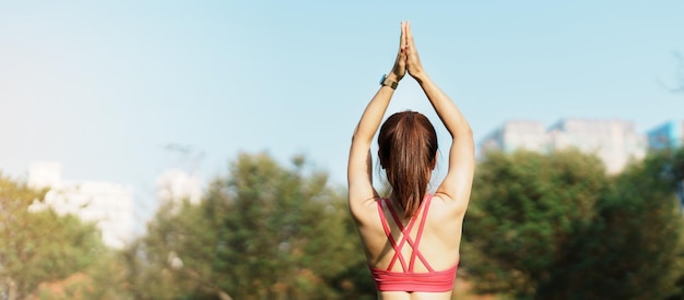 Junge erwachsene Frau in Sportkleidung beim Yoga im Park Gesunde Frau im Freien sitzend auf Gras und Meditation mit Lotus-Pose in morgendlichen Wellness-Fitness-Übungen und Work-Life-Balance-Konzepten