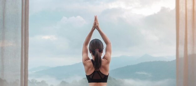 Junge erwachsene Frau in Sportkleidung, die Yoga macht und den Körper gegen den Blick auf die Berge dehnt, gesunde Frauenmeditation am Morgen. Wellness-, Fitness-, Vitalitäts-, Bewegungs- und Work-Life-Balance-Konzepte