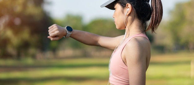 Junge erwachsene Frau prüft Zeit und Cardio-Herzfrequenz auf Sport-Smartwatch während des Laufens im Park im Freien, Läuferfrau, die am Morgen joggt. Bewegung, Technologie, Lebensstil und Training