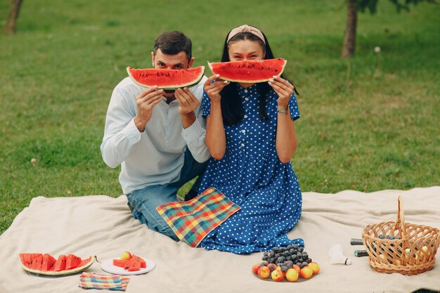 Junge erwachsene Frau und Mann paar picknicken auf der grünen Graswiese im Park, die Spaß haben und mit Wassermelone lächeln.