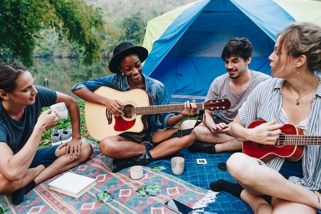 junge erwachsene freunde im camping spielen gitarre und ukulele und singen zusammen im freien