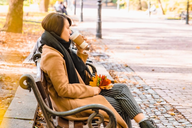 Junge erwachsene Modefrau, die in der Herbstsaison auf der Stadtparkbank sitzt