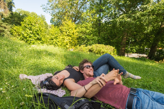 Foto junge erwachsene paare, die sich auf üppigem grünem gras im park, entspannend hinlegen und umfassen
