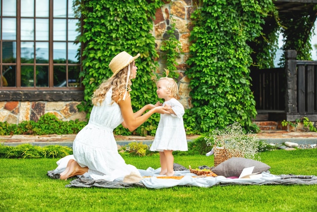 Junge erwachsene schöne frau in einem kleid mit einer mädchentochter auf einem picknick im garten am haus