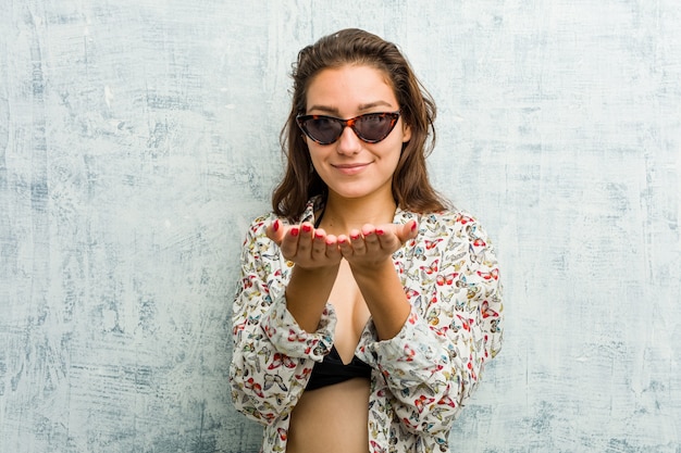 Junge europäische Frau, die Bikini trägt, der etwas mit Handflächen hält