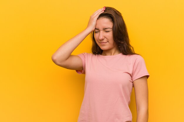 Junge europäische Frau getrennt über dem gelben Vergessen etwas, Stirn mit Palme schlagend und schließen Augen.