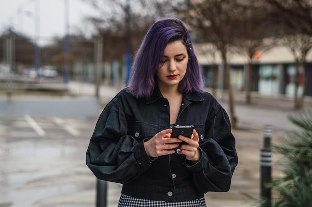 Junge europäische Frau mit lila Haaren, die auf die Straße geht und SMS auf ihrem Telefon schreibt