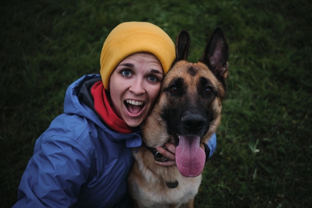 Junge europäische weiße Frau sitzt im grünen Gras und umarmt ihren Deutschen Schäferhund