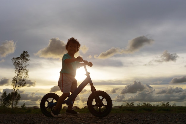 Junge fährt bei Sonnenuntergang auf einem bewölkten Himmel Fahrrad