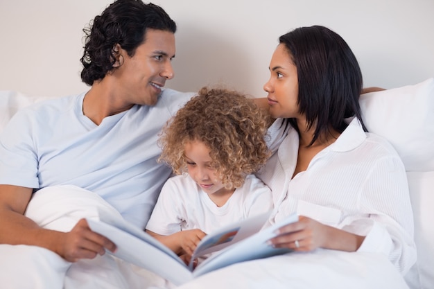 Junge Familie, die auf dem Bett liest ein Buch sitzt