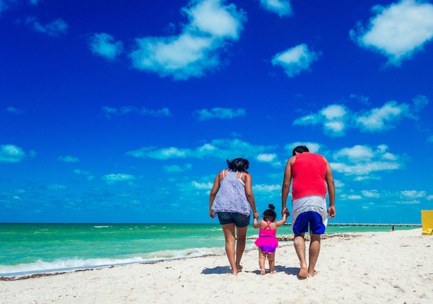 Junge Familie, die auf dem Sand am Ufer des Strandes geht. Eltern halten die Hand ihres Babys in der Nähe des Meeres