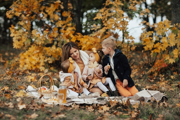 Junge Familie, die auf einer Picknickdecke sitzt und ein schönes Herbstpicknick in der Natur umarmt und genießt.