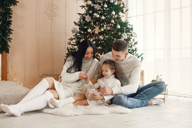 Junge Familie, die nahe Weihnachtsbaum sitzt und zusammen feiert