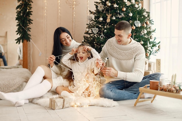 Junge Familie, die nahe Weihnachtsbaum sitzt und zusammen feiert